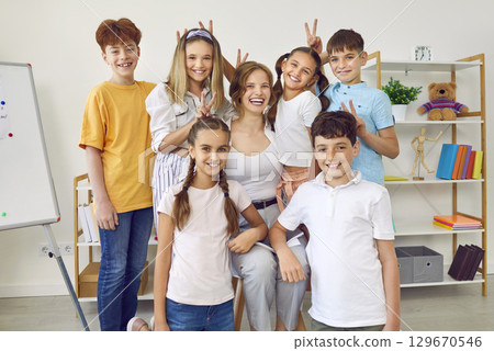 Cheerful little students making horns with their fingers and their friendly young teacher. Cheerful little students making horns with their fingers and their friendly young teacher. 129670546