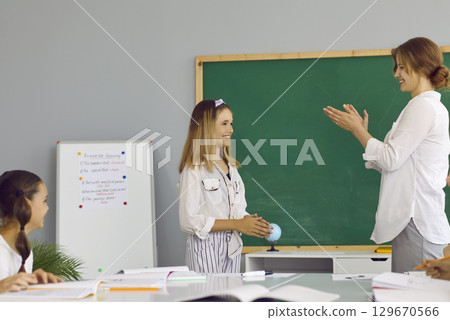 Beautiful, young, smiling schoolmistress applauds the excellent response of her joyful, happy, sweet student. Beautiful, young, smiling schoolmistress applauds the excellent response of her joyful, happy, sweet student. 129670566