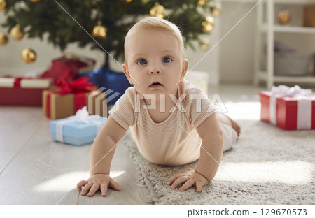 Happy small baby, first Christmas eve child creeping on warm carpet near decorated festive tree Happy small baby, first Christmas eve child creeping on warm carpet near decorated festive tree 129670573