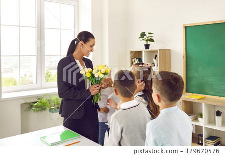 Little children congratulate their beloved woman teacher and give flowers stand in school room Little children congratulate their beloved woman teacher and give flowers stand in school room 129670576