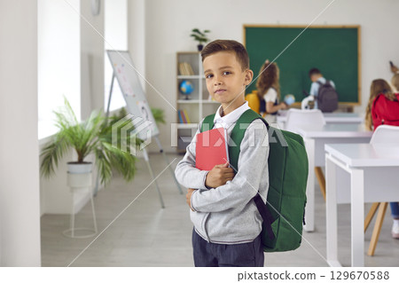 Portrait of a little schoolboy with a backpack and notebook standing in the classroom 129670588