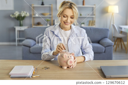 Happy woman putting coin in piggybank to enjoy saving money, managing household budget at home Happy woman putting coin in piggybank to enjoy saving money, managing household budget at home 129670612