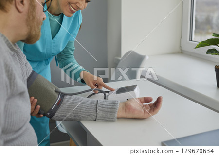 Nurse or doctor uses a tonometer to measure the blood pressure of her senior patient Nurse or doctor uses a tonometer to measure the blood pressure of her senior patient 129670634