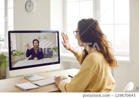 Happy smiling woman waving hand saying hello having online video call with colleague or a friend. 129670645