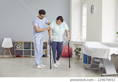 Physiotherapist helps woman patient who walks with crutches during rehabilitation at clinic Physiotherapist helps woman patient who walks with crutches during rehabilitation at clinic 129670652