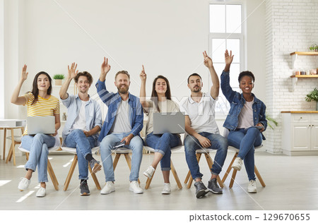 Business people sitting in row on seminar training raising their hands up knowing the answer. Business people sitting in row on seminar training raising their hands up knowing the answer. 129670655
