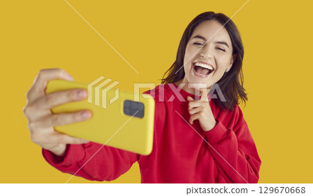 Happy young girl brunette takes selfie on isolated yellow background. 129670668