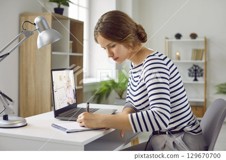 Young woman is learning online using laptop, listening to reading and writing her notes. Young woman is learning online using laptop, listening to reading and writing her notes. 129670700