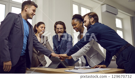 Multiracial team of happy young business people stacking hands after work meeting 129670732