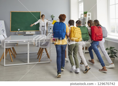 Group of happy children who have missed their school teacher are running to hug her 129670742