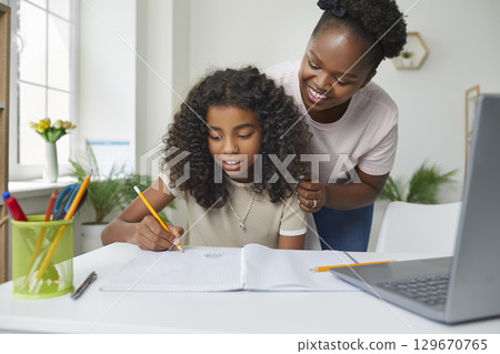 Happy young African American mother is helping her daughter with school homework 129670765
