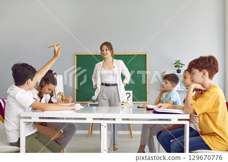 Beautiful, young, smiling teacher asks questions to her students at modern private school. 129670776