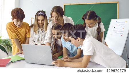 Children in class at elementary school with teacher working together on laptop in classroom. 129670779