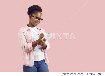 Smiling young African American woman writing down notes in clipboard Smiling young African American woman writing down notes in clipboard 129670786