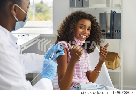 Happy teenage girl showing thumbs up gesture while being immunized against viral infections. Happy teenage girl showing thumbs up gesture while being immunized against viral infections. 129670809