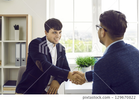 Two people sitting at an office desk, making a business deal and exchanging handshakes 129670822