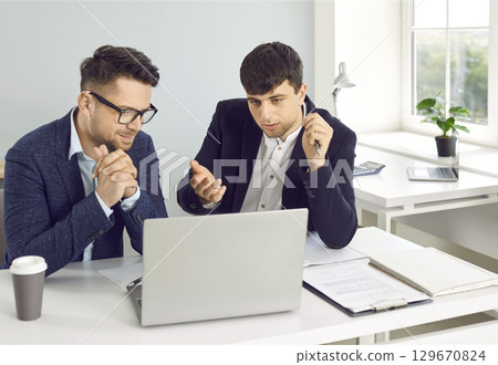 Two business men at work in office. Two employers sitting with laptop computer and talking. 129670824
