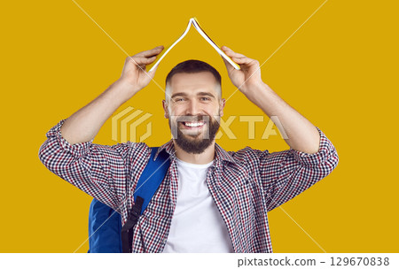 Portrait of happy male college or university student holding book above his head like roof Portrait of happy male college or university student holding book above his head like roof 129670838