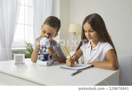 Two little school children take notes while looking at something under microscope Two little school children take notes while looking at something under microscope 129670841