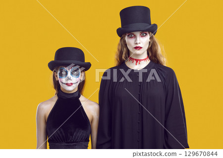 Serious mother and daughter in Halloween outfits looking at you waiting for trick or treat. Serious mother and daughter in Halloween outfits looking at you waiting for trick or treat. 129670844