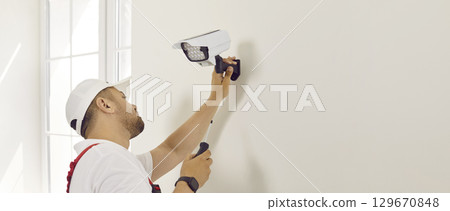 Worker repairing or installing video surveillance camera on white copy space wall Worker repairing or installing video surveillance camera on white copy space wall 129670848