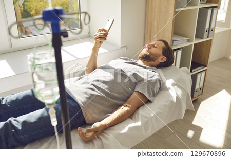 Male patient using mobile phone while getting intravenous vitamin therapy at clinic 129670896