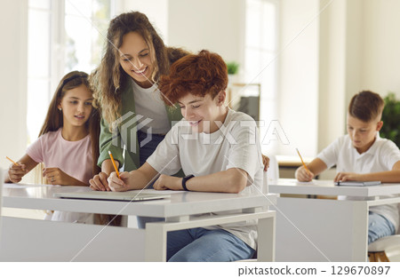 Woman teacher in junior high school helping a boy during a lesson in the classroom. 129670897