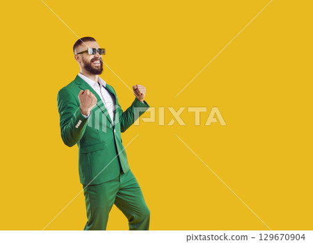 Overjoyed showman businessman in green suit and sunglasses showing yes gesture and smiling. 129670904