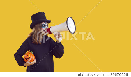 Kid in spooky Halloween costume makes announcement through megaphone on color copy space background Kid in spooky Halloween costume makes announcement through megaphone on color copy space background 129670906