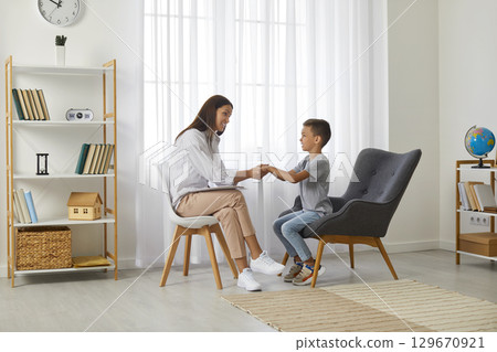 Cute boy and female psychologist holding hands together 129670921