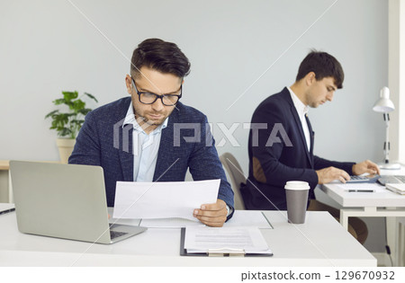 Busy corporate employees sitting at office desks and working with business documents 129670932
