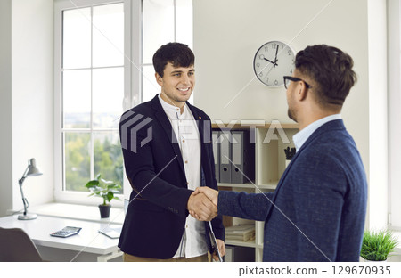 Smiling businessman manager shaking hand to his partner after meeting in modern office. Smiling businessman manager shaking hand to his partner after meeting in modern office. 129670935