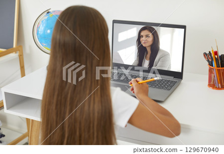 Young female teacher having video conference call with a child girl pupil using webcam. Young female teacher having video conference call with a child girl pupil using webcam. 129670940