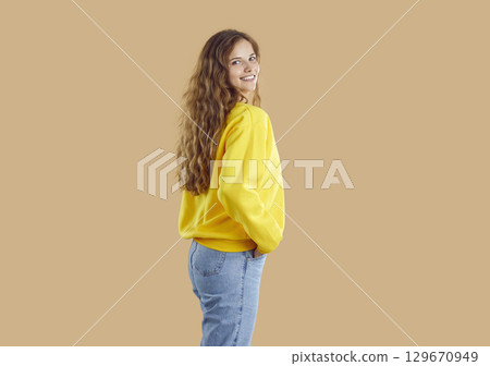 Happy girl in yellow sweatshirt and blue jeans posing isolated on beige background Happy girl in yellow sweatshirt and blue jeans posing isolated on beige background 129670949
