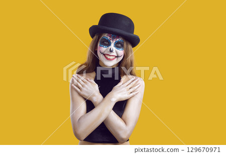 Cheerful joyful preteen girl with cool Halloween makeup smiling on orange background in studio. Cheerful joyful preteen girl with cool Halloween makeup smiling on orange background in studio. 129670971