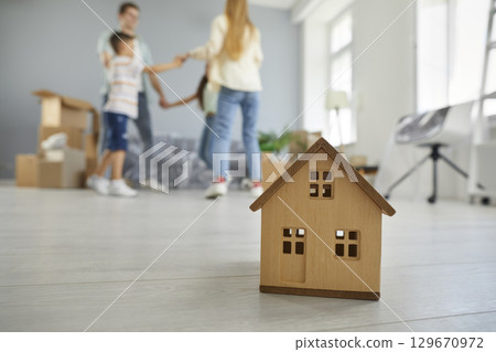 Wooden house model in front young family with children dancing after buying real estate Wooden house model in front young family with children dancing after buying real estate 129670972
