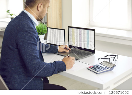 Busy concentrated male financier working in office with Excel spreadsheets and calculator. 129671002