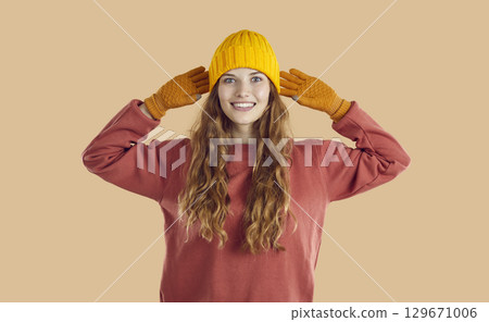 Cheerful beautiful young woman posing in autumn clothes hat and gloves on light beige background. 129671006