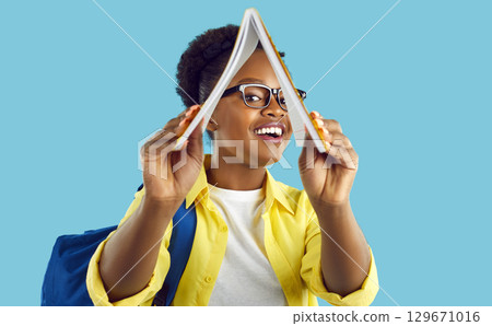 Funny african american female student looking at you from open book on light blue background. 129671016