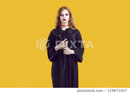 Portrait of woman with bloody creepy makeup holding black rose in her hands and looking at camera. 129671057
