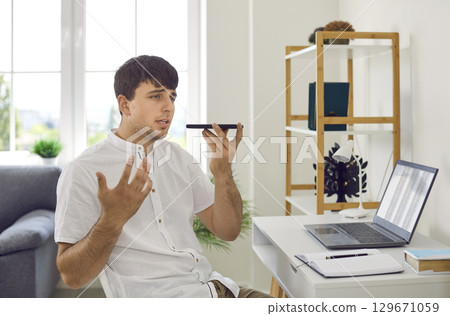 Young businessman using his mobile to talk on speaker phone or send voice messages 129671059