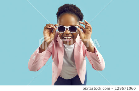 Portrait of cheerful young African American woman in pink jacket and trendy sunglasses 129671060