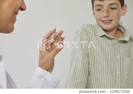 Audiologist gives a modern hearing aid to a child patient with some hearing loss 129671080