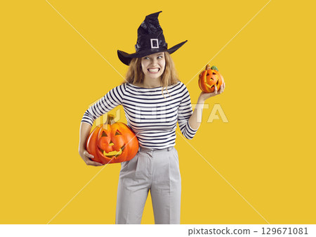 Young woman in witch hat holding Halloween pumpkins and making funny, scary face Young woman in witch hat holding Halloween pumpkins and making funny, scary face 129671081