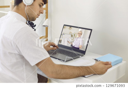 Adult student taking notes during his online lesson with a remote English teacher Adult student taking notes during his online lesson with a remote English teacher 129671093