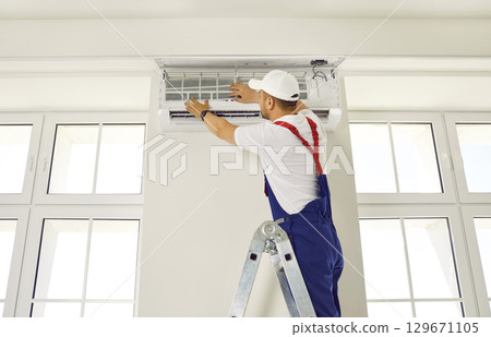 Worker installs ventilation system in appartment room or office from ladder. 129671105