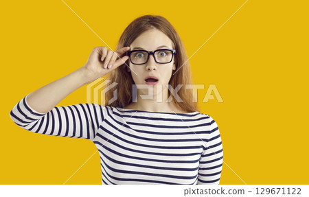 Beautiful young woman in glasses looking at something with funny, surprised face expression 129671122