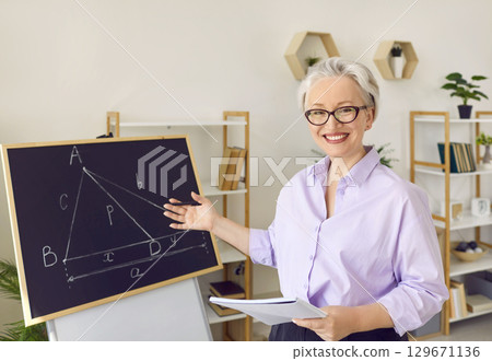 Portrait of a happy online maths teacher smiling and pointing at the school blackboard 129671136