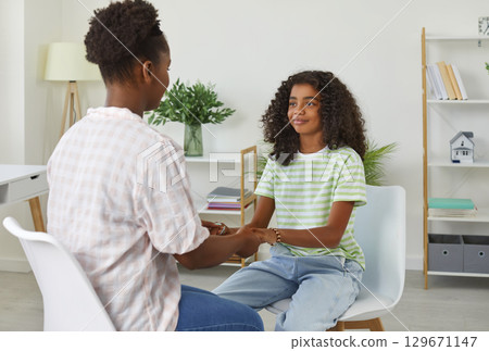 African american woman psychologist holding hands teen girl sitting in front of her at school. African american woman psychologist holding hands teen girl sitting in front of her at school. 129671147