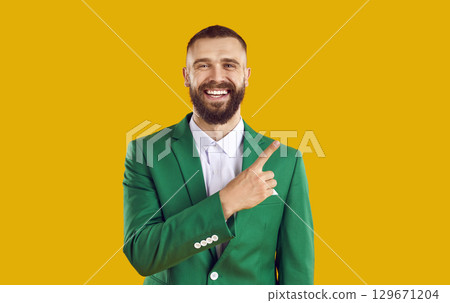 Cheerful bearded man in green suit is pointing with his finger to side for advertising space. 129671204